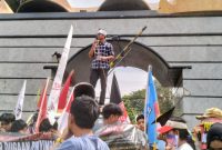 Seorang orator Aliansi Lampung Bersatu Awasi Kebijakan dan Anggaran berorasi menggunakan pengeras suara di depan gerbang Kantor DPRD Provinsi Lampung, Kamis 25/6/2026. 