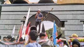 Seorang orator Aliansi Lampung Bersatu Awasi Kebijakan dan Anggaran berorasi menggunakan pengeras suara di depan gerbang Kantor DPRD Provinsi Lampung, Kamis 25/6/2026. 