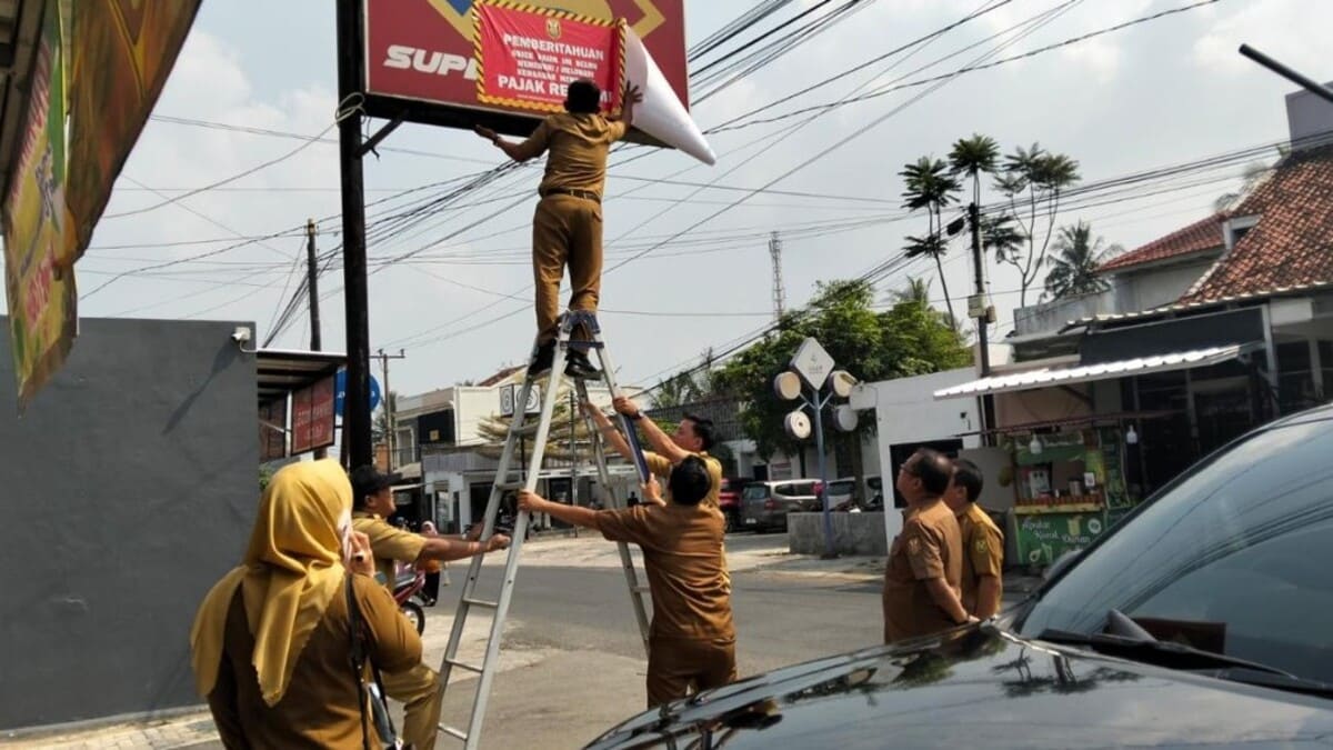 Petugas Bapenda Kota Bandar Lampung memasang stiker pemberitahuan kepada wajib pajak reklame yang menunggak di wilayah Rajabasa, Selasa 30/6/2026. Foto: Proyeksi.id